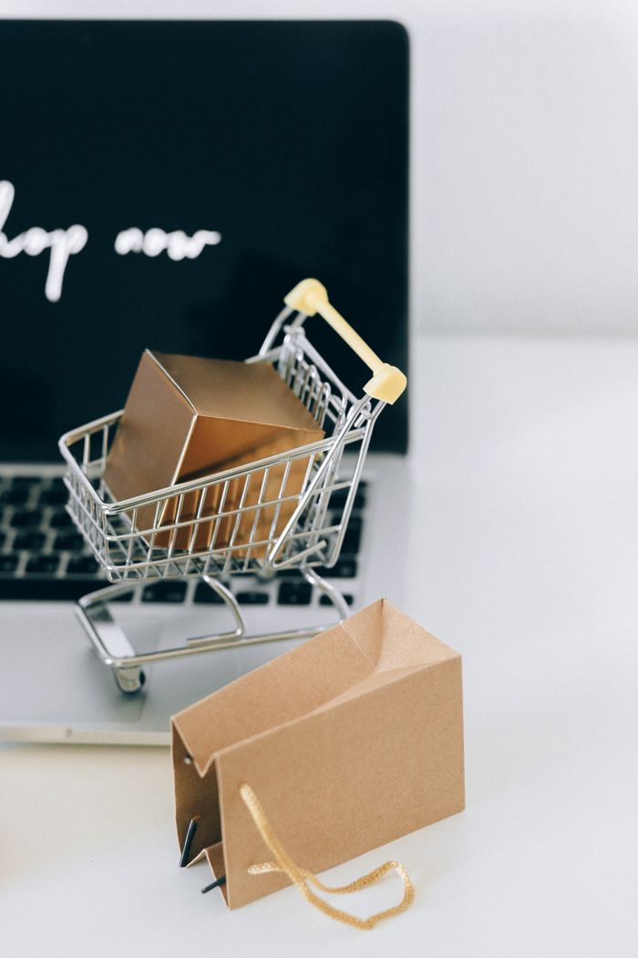creative-01 A miniature shopping cart with a parcel on a laptop symbolizes online shopping and e-commerce.