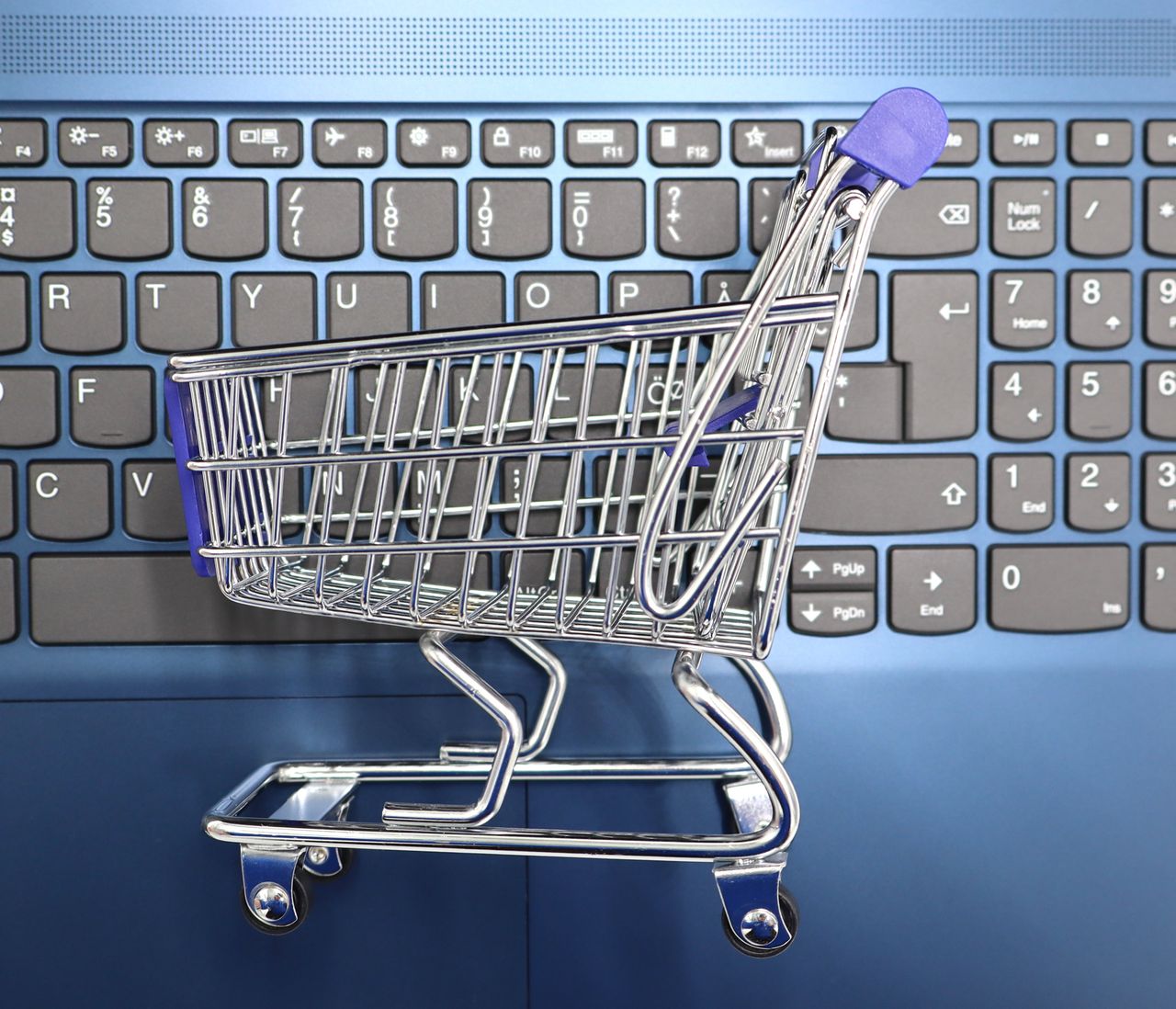 Services-01 A miniature shopping cart placed on a laptop keyboard symbolizing online shopping and e-commerce.