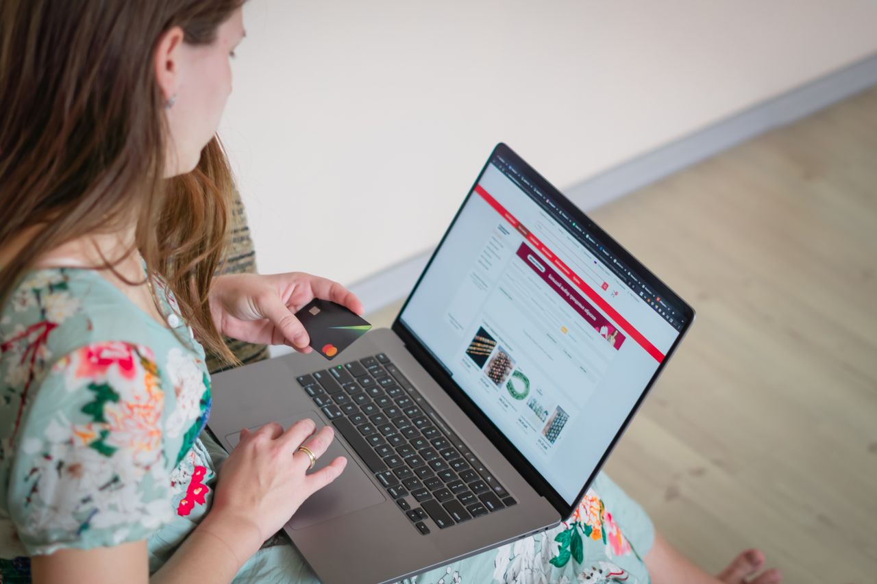 creative Woman in floral dress shopping online with a laptop and credit card indoors.