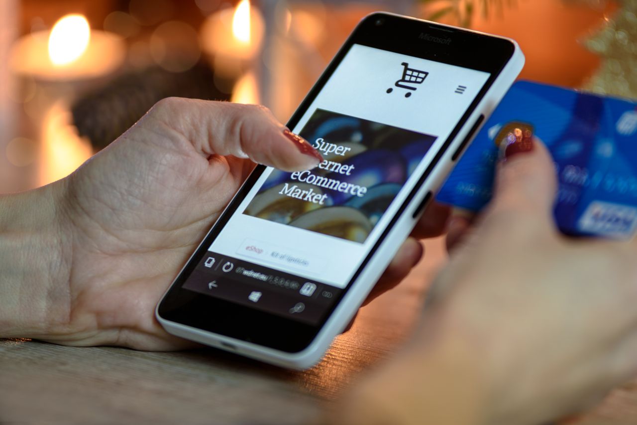 digital Woman using smartphone for online shopping with credit card in hand, festive background lighting.